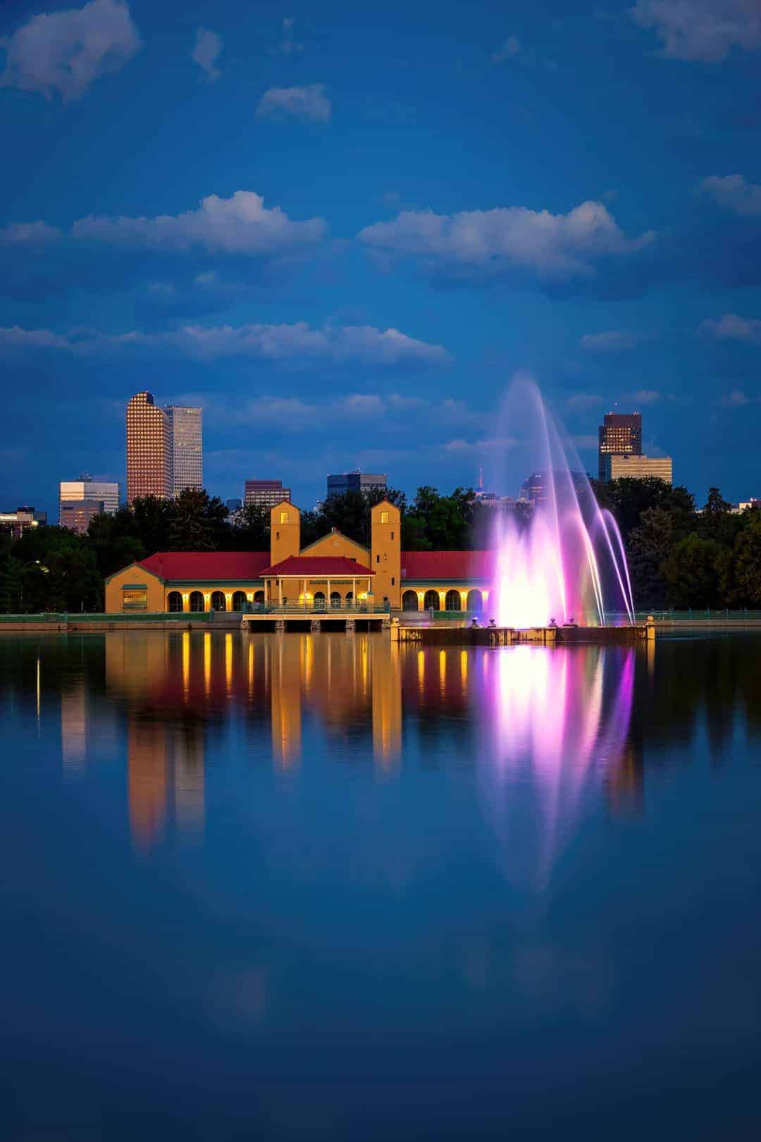 Downtown Denver skyline and City Park fountain reflected in the still water of Ferril Lake during blue hour just before sunrise.