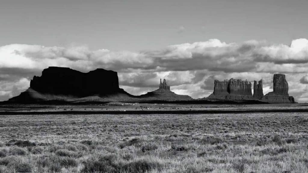 Black and white photo of aternoon clouds building over the rock formations of Monument Valley, Arizona.