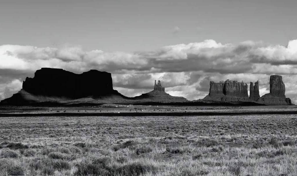 Black and white photo of aternoon clouds building over the rock formations of Monument Valley, Arizona.