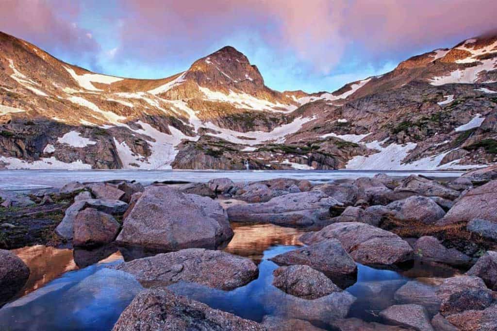 The first rays of dawn cast the sky pink as they fall across Mt. Toll and the still partially frozen surface of Blue Lake on this early July morning in Colorado's Indian Peaks Wilderness.