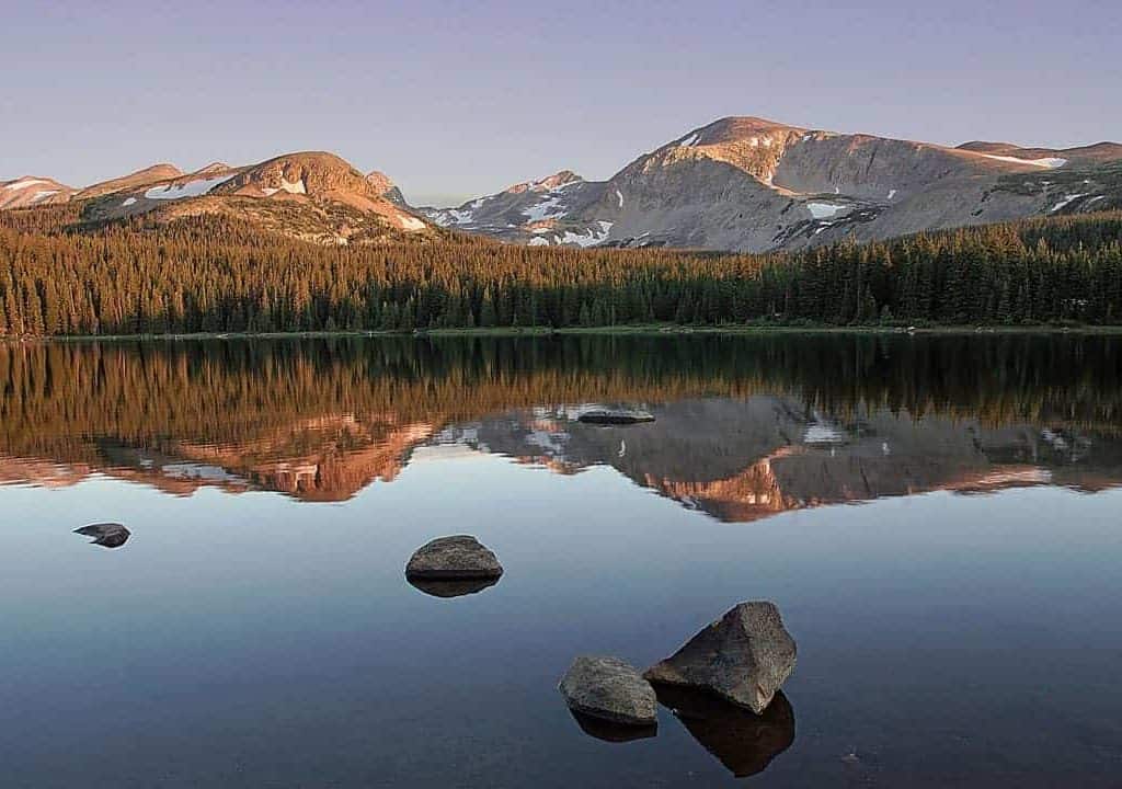 Brainard Lake in the Indian Peaks Wilderness is calm and smooth as glass at sunrise on this June morning, reflecting the surrounding mountains in the dawn light.
