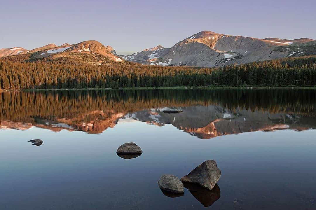 Brainard Lake in the Indian Peaks Wilderness is calm and smooth as glass at sunrise on this June morning, reflecting the surrounding mountains in the dawn light.