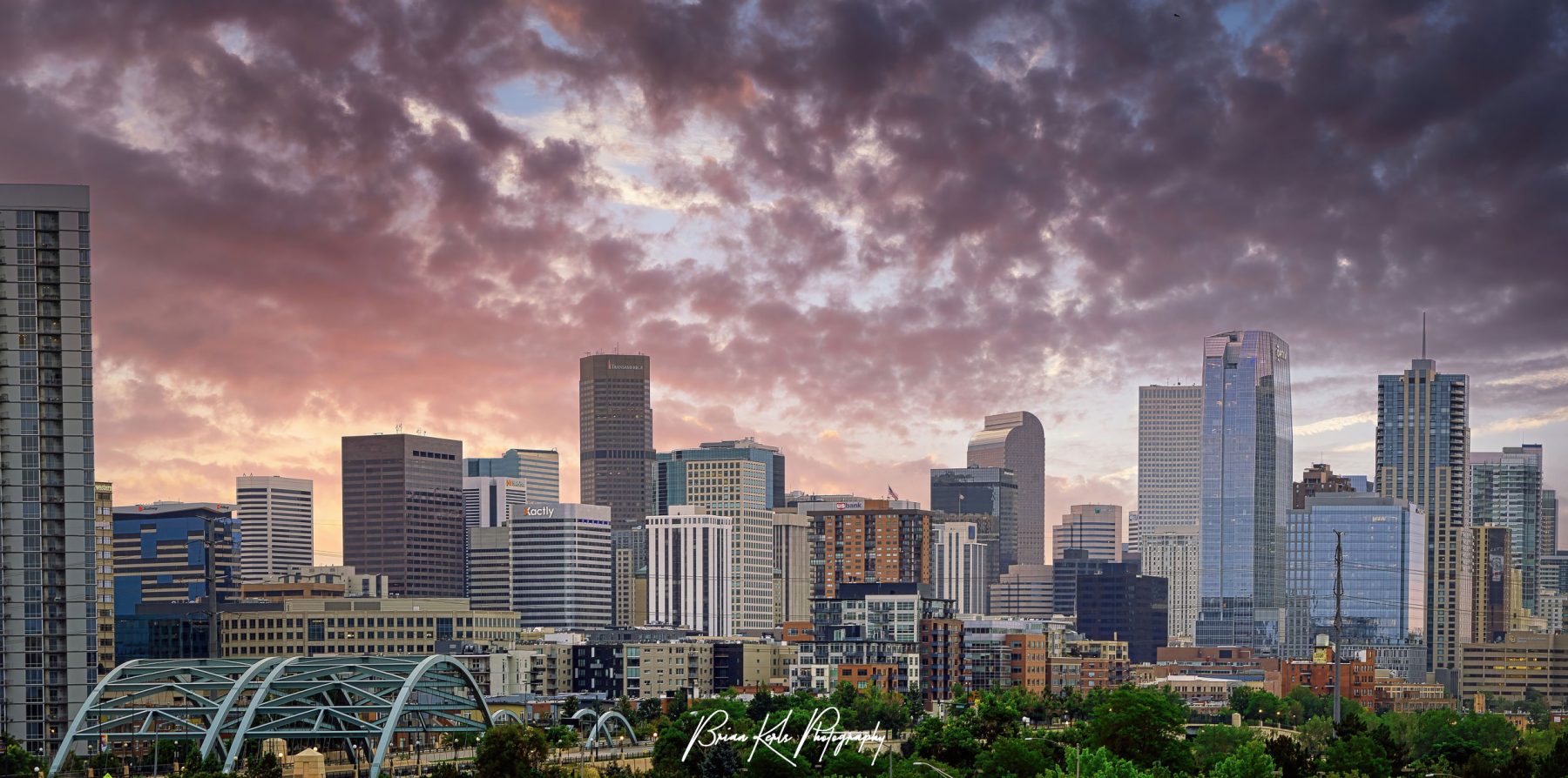 Multi-image panorama of the downtown Denver skyline under a colorful summer sunrise sky.