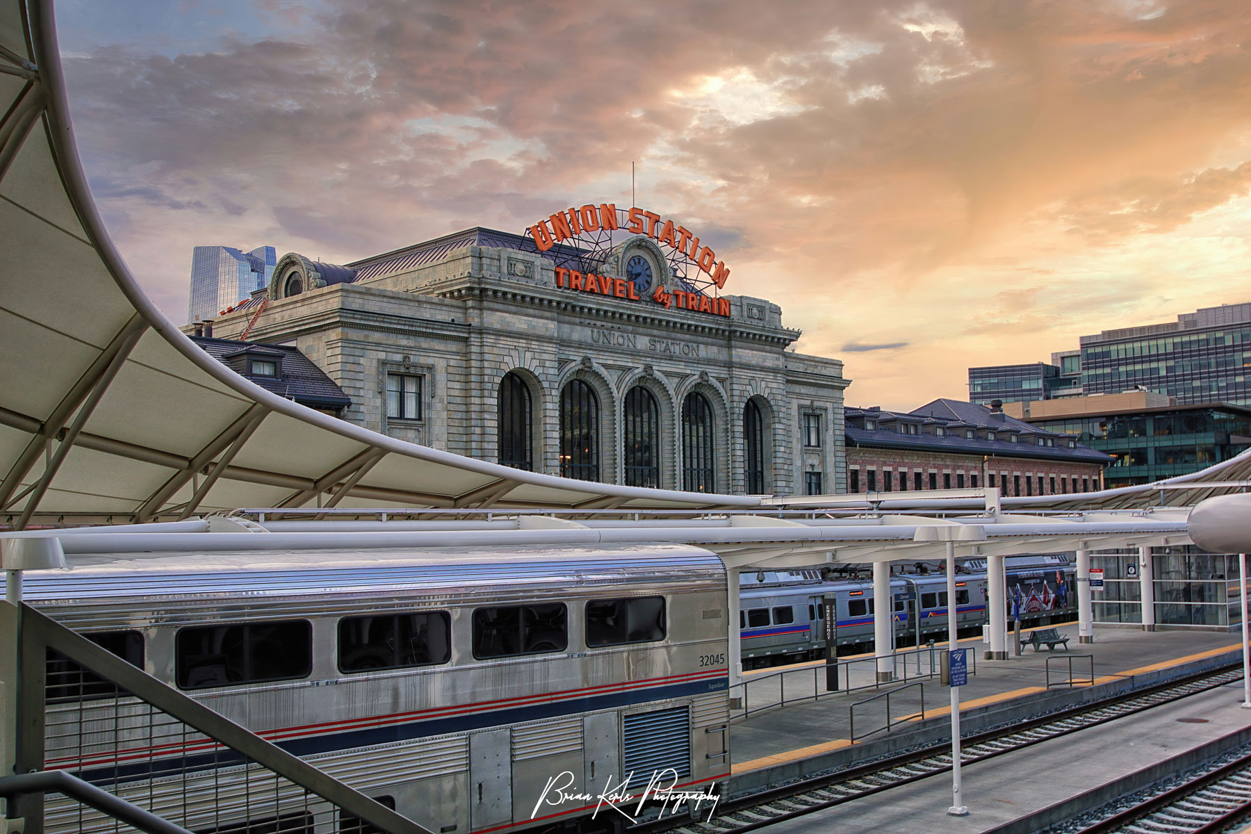 The distinctive modern structure of the new light rail concourse contrasts with original vintage Union Station facade under a colorful early morning sky at sunrise in downtown Denver, Colorado.