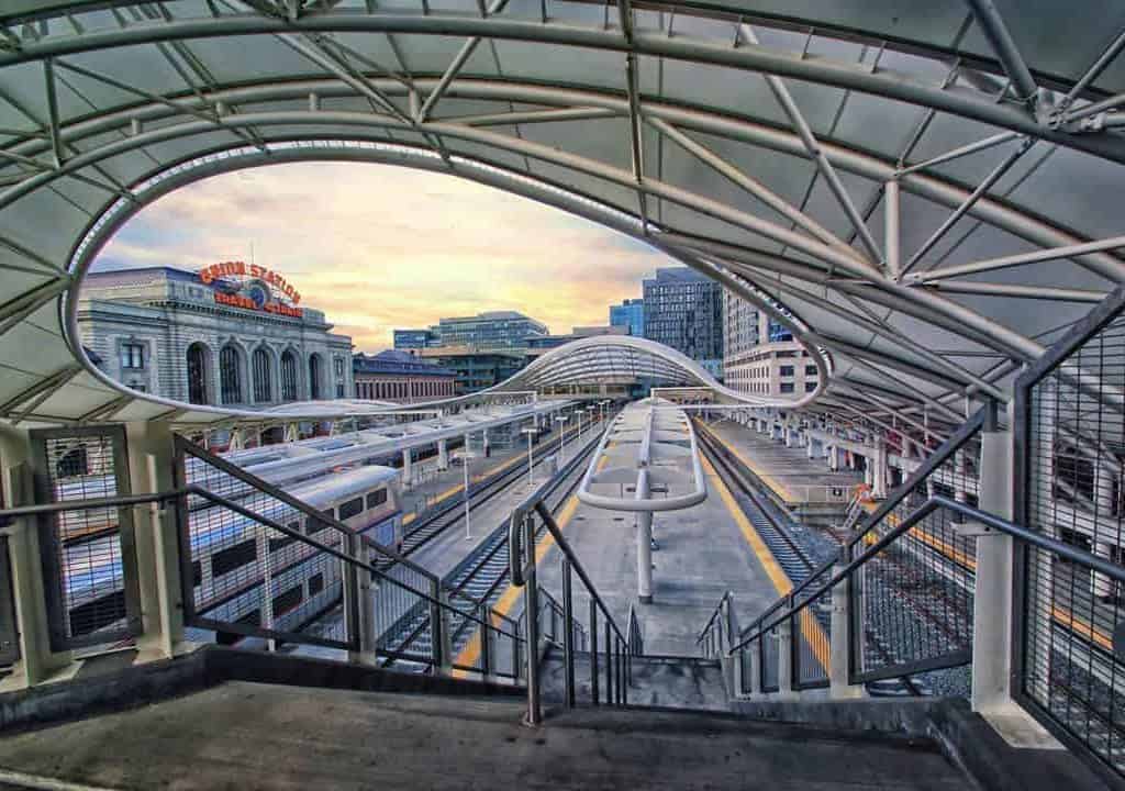 The modern architecture of the light rail concourse meets the original vintage Union Station facade under a colorful early morning sky at sunrise in downtown Denver, Colorado.