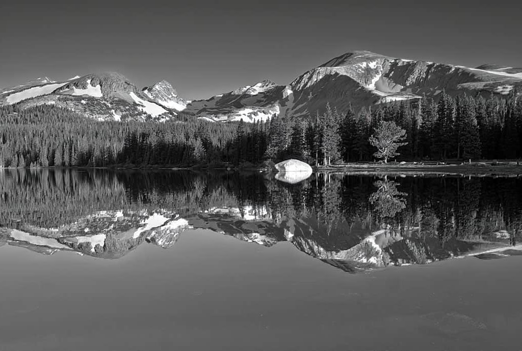 Brainard Lake in the Indian Peaks Wilderness is calm and smooth as glass at sunrise on this June morning, reflecting a perfect mirror image of the surrounding mountains bathed in the dawn light.