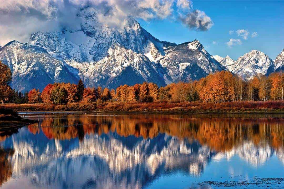 With its summit shrouded in clouds, Mount Moran is reflected in the still water of the Snake River at Oxbow Bend on a cool fall morning in Grand Teton National Park, Wyoming.