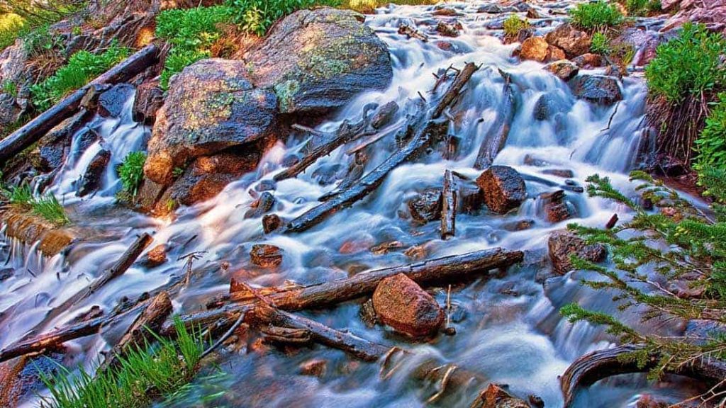 Swiftly flowing stream below Dream Lake in Rocky Mountain National Park, CO cascades over boulders and fallen logs.