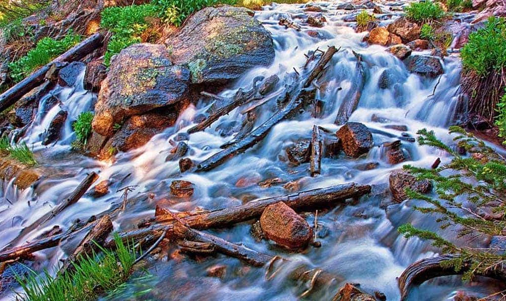 Swiftly flowing stream below Dream Lake in Rocky Mountain National Park, CO cascades over boulders and fallen logs.