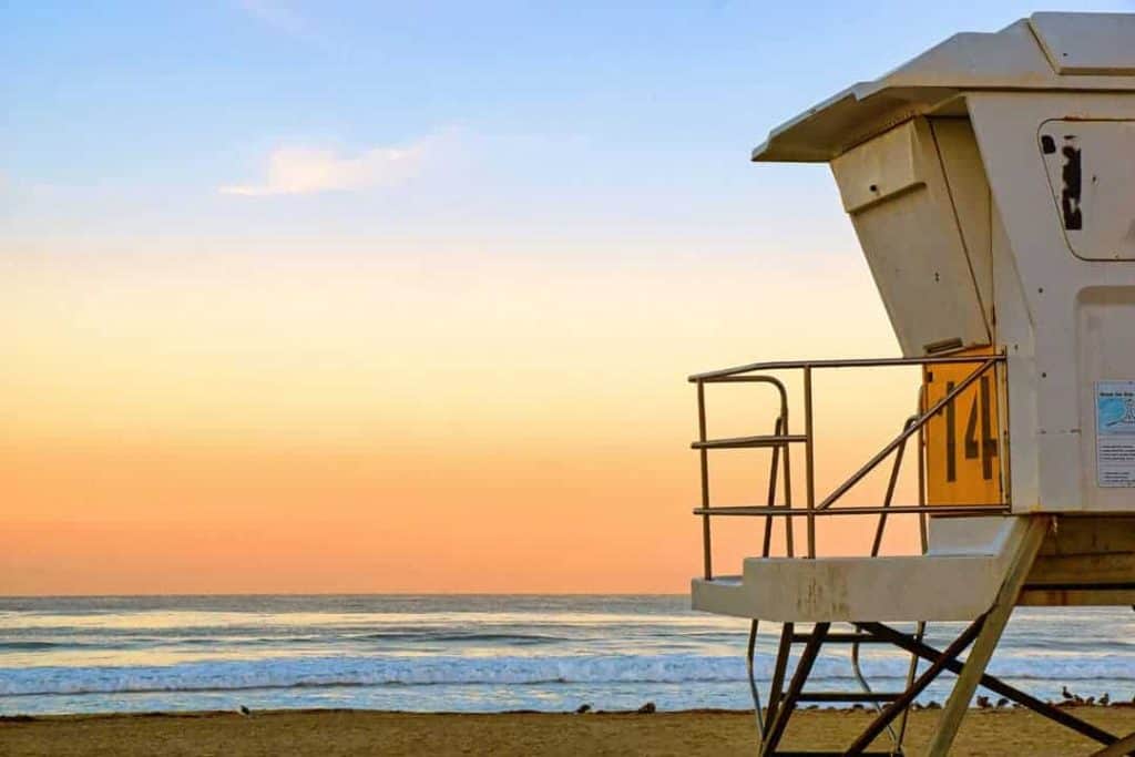The horizon glows orange over the Pacific ocean in front of a lifeguard tower at sunrise on Mission Beach in San Diego, California.