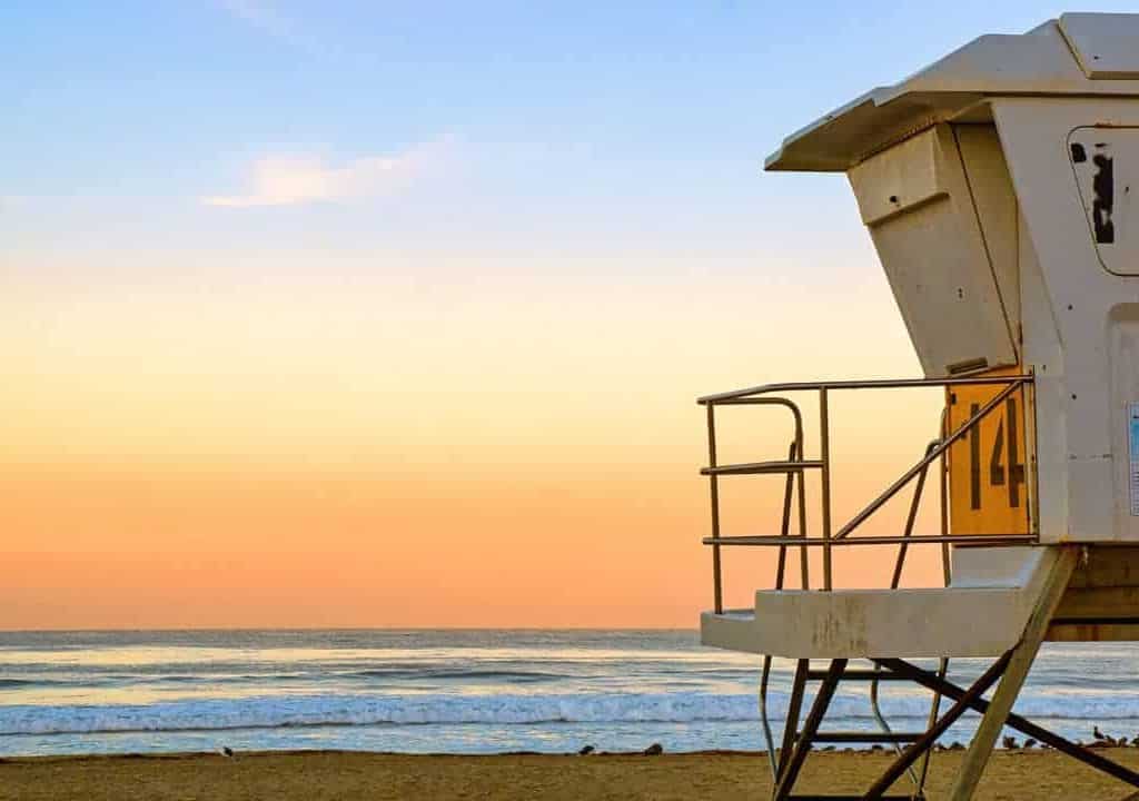 The horizon glows orange over the Pacific ocean in front of a lifeguard tower at sunrise on Mission Beach in San Diego, California.