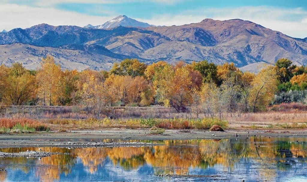 Coloful autumn trees reflected in the still water of Sawhill Ponds near Boulder, Colorado with Mt. Evans and the Front Range mountains providing a dramatic backdrop.