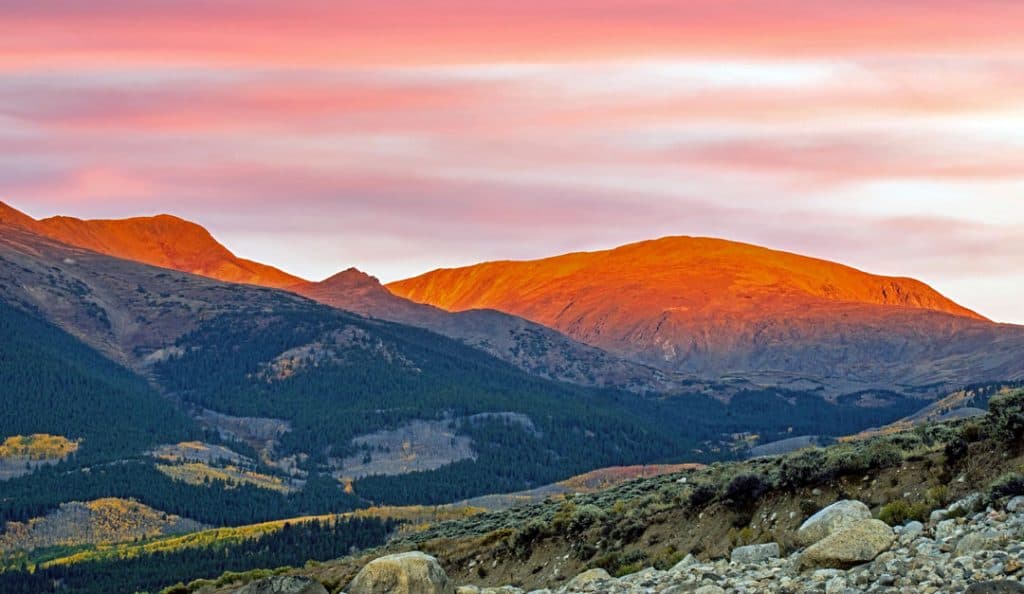 The peaks of the Sawatch Range in Colorado glow red in the dawn light early on an autumn morning.