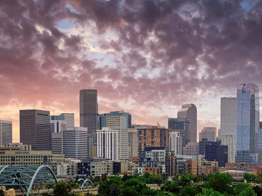 A multi-image panorama of the downtown Denver skyline under a colorful summer sunrise sky.