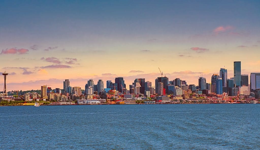 Looking across Elliott Bay from the Bainbridge Island Ferry, an early summer sunset colors the sky and highlights the Space Needle and the striking skyline of downtown Seattle, Washington.