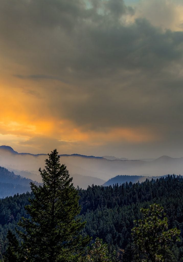 The lingering smoke from a prescribed forest service burn in the Rocky Mountains of Colorado hangs in the valley as the sky is lit up at sunset.