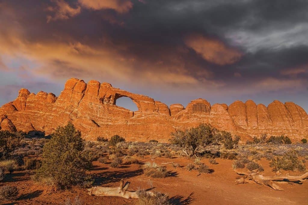Skyline Arch glows under a colorful winter sunset sky. This large natural arch high in a sandstone wall in the Devil's Garden area of Arches National Park, Utah is one of the park's more popular landmarks.