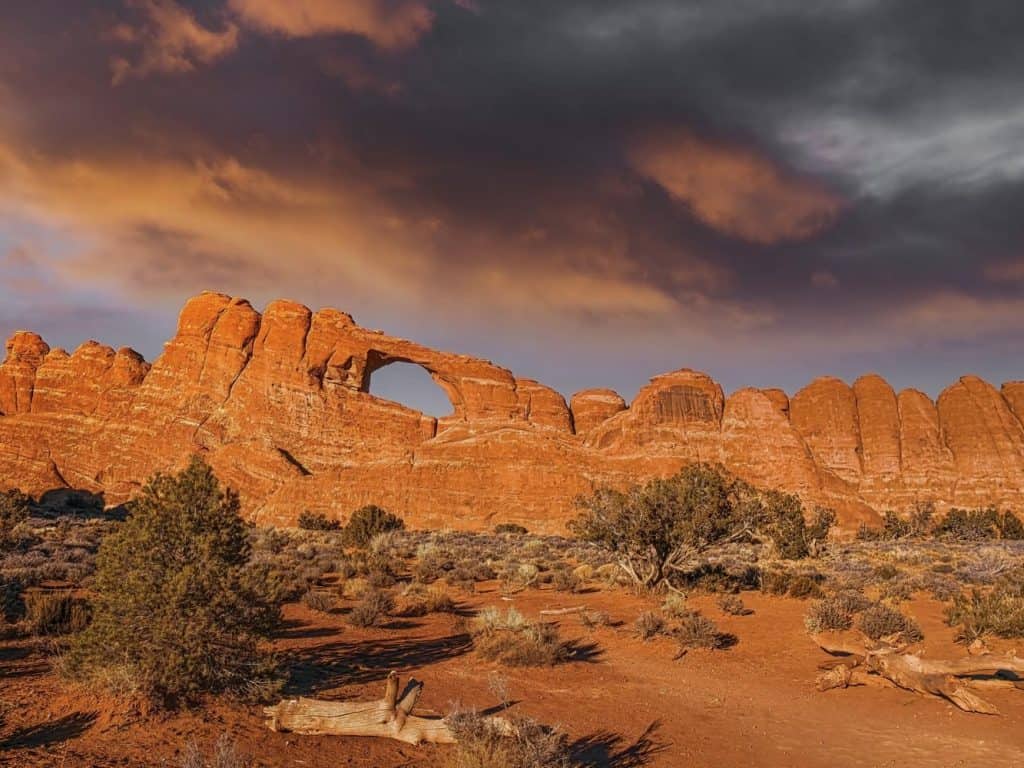 Skyline Arch glows under a colorful winter sunset sky. This large natural arch high in a sandstone wall in the Devil's Garden area of Arches National Park, Utah is one of the park's more popular landmarks.