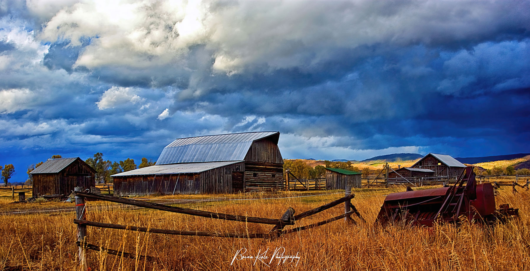 A few rays of sunlight break through early evening storm clouds and illuminate the barns along Mormon Row near Grand Teton National Park, Wyoming