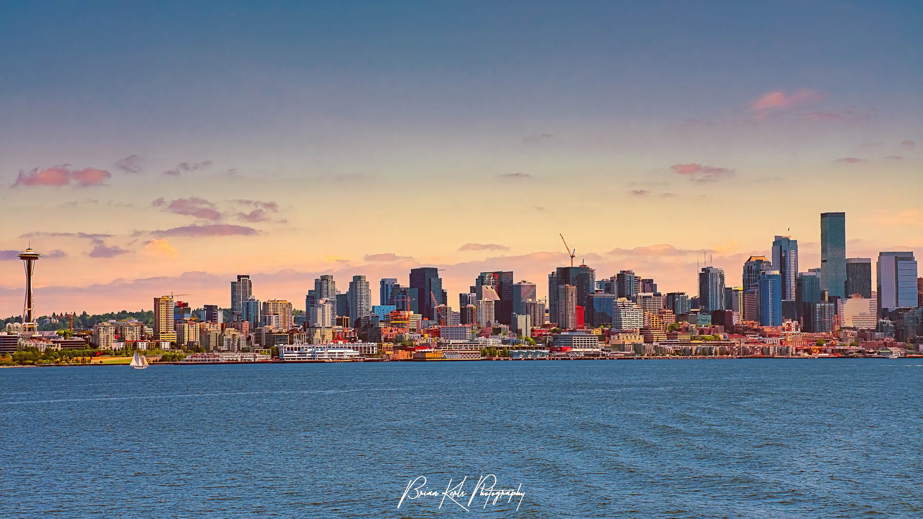 Looking across Elliott Bay from the Bainbridge Island Ferry, an early summer sunset colors the sky and highlights the Space Needle and the striking skyline of downtown Seattle, Washington.