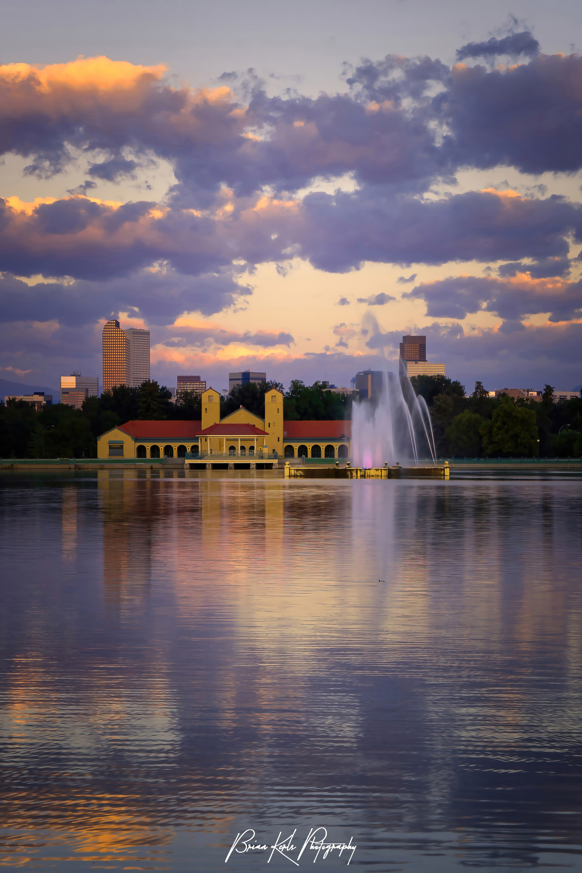 Downtown Denver skyline and a colorful sunrise sky reflected in the calm water of Ferril Lake in City Park on a summer morning.