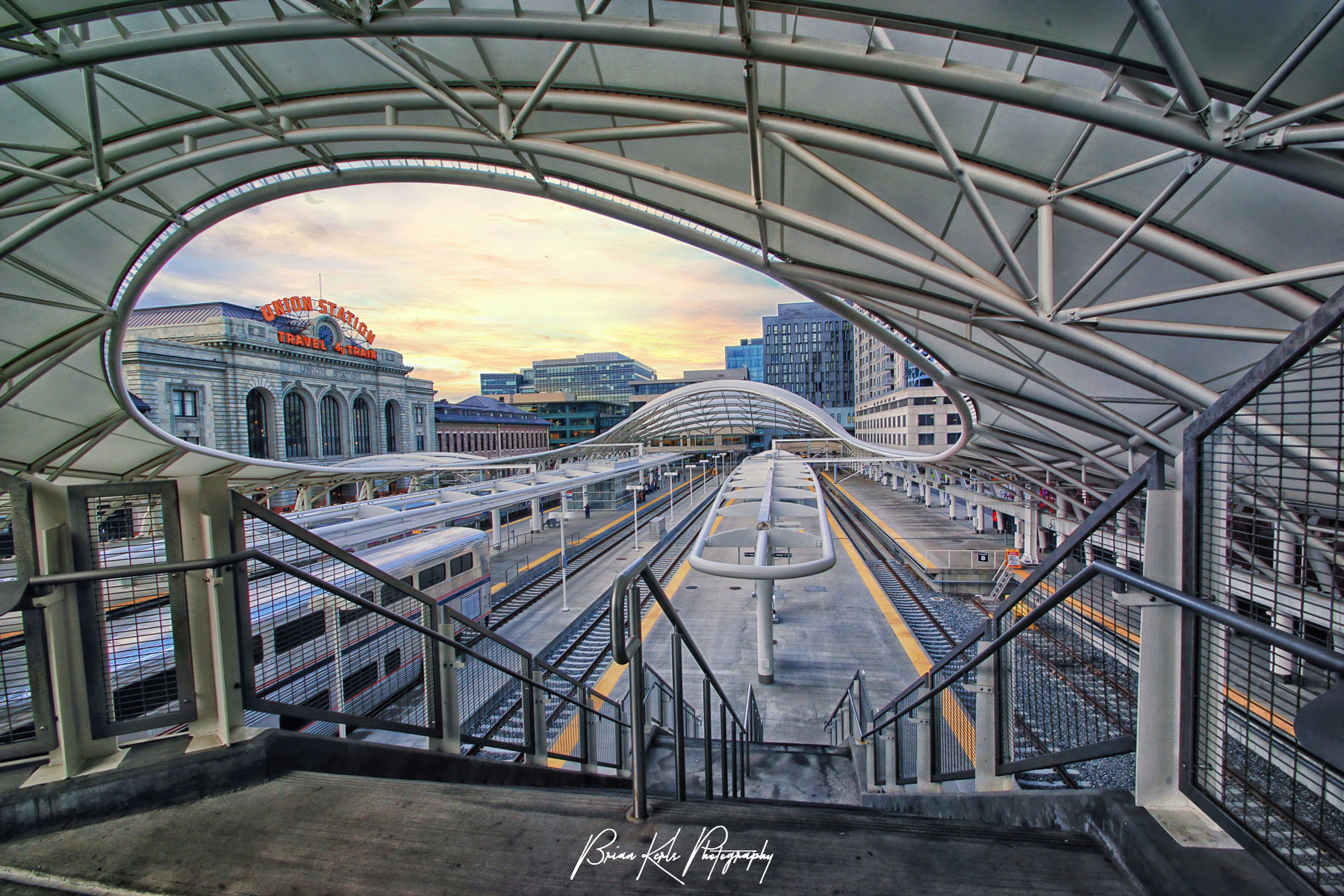 The modern architecture of the light rail concourse meets the original vintage Union Station facade under a colorful early morning sky at sunrise in downtown Denver, Colorado.