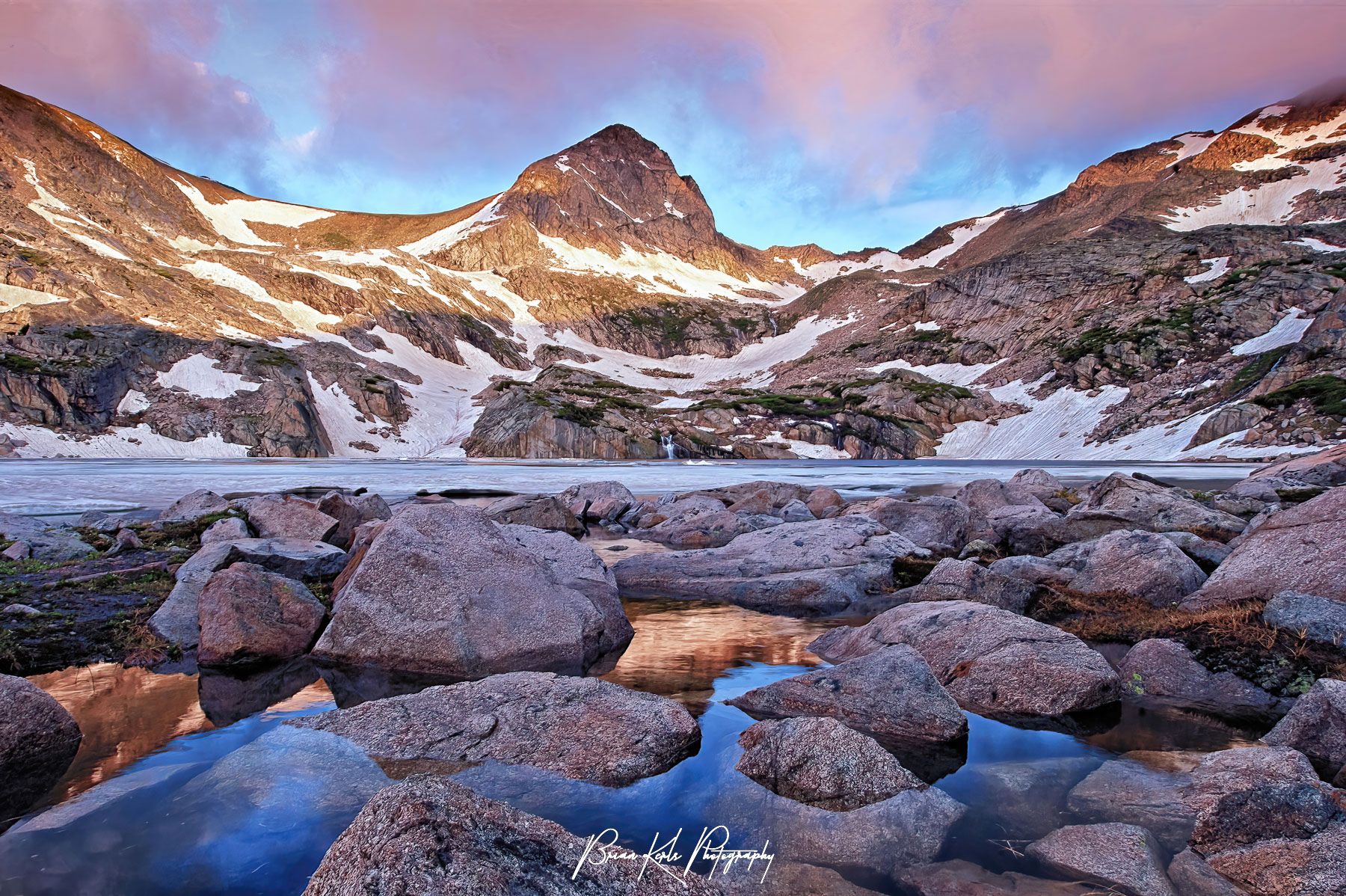 The first rays of dawn cast the sky pink as they fall across Mt. Toll and the still partially frozen surface of Blue Lake on this early July morning in Colorado's Indian Peaks Wilderness.