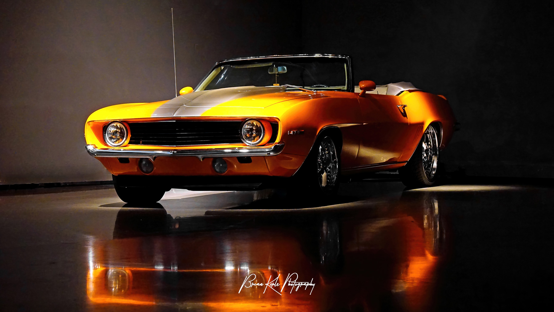 A restored , classic 1969 Chevrolet Camaro convertible with a bold stripe down its hood. The chrome detailing and round headlights add to its vintage appeal.