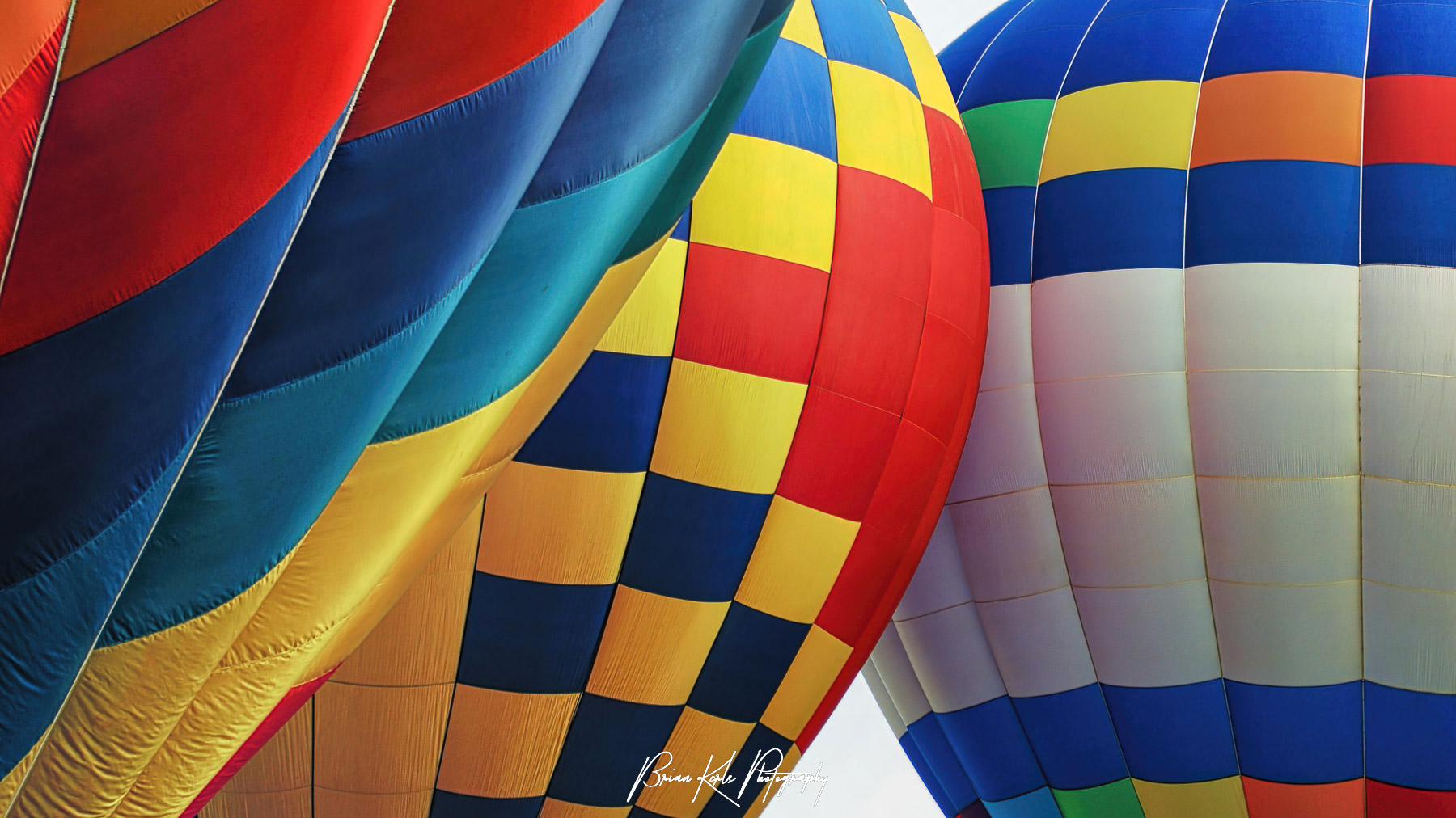 Three brightly colored hot air balloons preparing for lift off at the Colorado Springs Hot Air Balloon Festival.