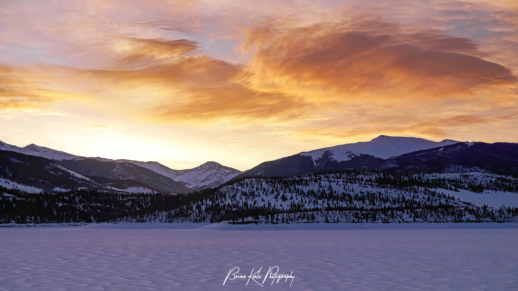 Colorful winter sunrise illuminates the peaks surrounding an icy and frozen Lake Dillon in Summit County, Colorado.