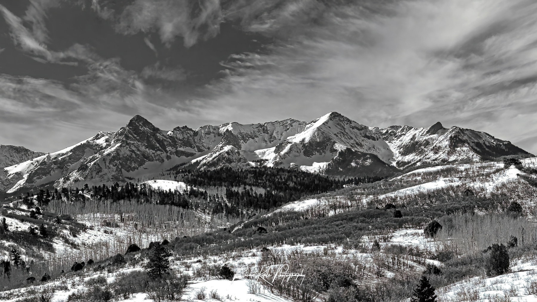 Dallas Divide is an iconic high mountain pass in Southwestern Colorado. It is famous for colorful autumn scenes of aspen forests agains the rugged peaks of the San Juans. While most often photographed in the fall, Dallas Divide also makes for a delightful winter mountain landscape. Here, black and white adds the perfect touch to the already stark winter environment and sweeping afternoon clouds add some drama to the blue sky.