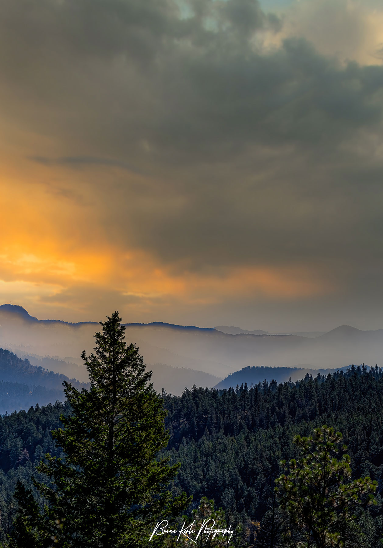 The lingering smoke from a prescribed forest service burn in the Rocky Mountains of Colorado hangs in the valley as the sky is lit up at sunset.