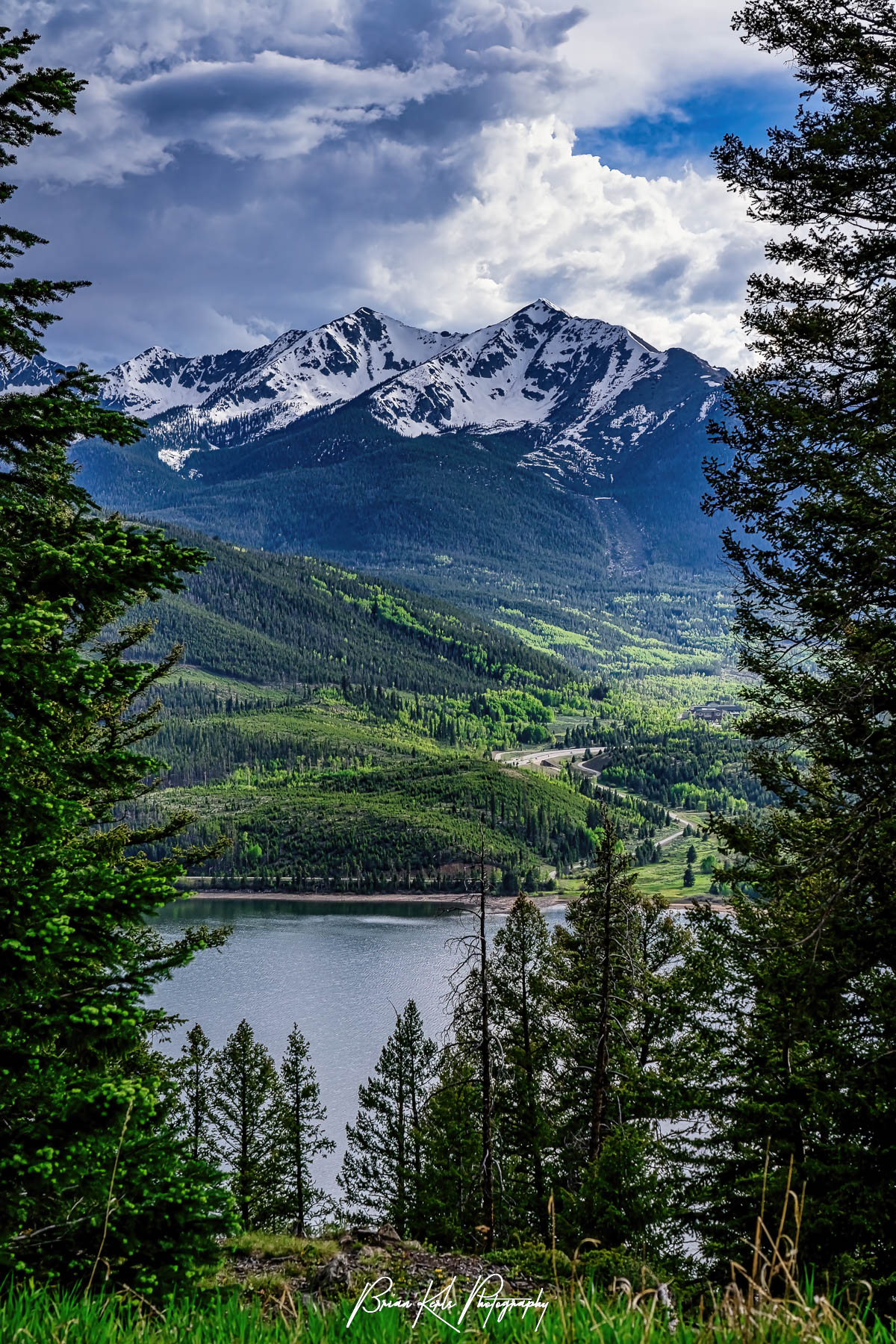 Towering evergreen trees naturally frame the peaks of the Ten Mile Range in Summit County, Colorado which remain snow-capped in contract to the bright green new spring growth blanketing the mountain sides. Composed on an early June day from along Swan Mountain Road overlooking Lake Dillon near the Sapphire Point Overlook as afternoon storm clouds build around Peak One (12,805') and Ten Mile Peak (12,933').