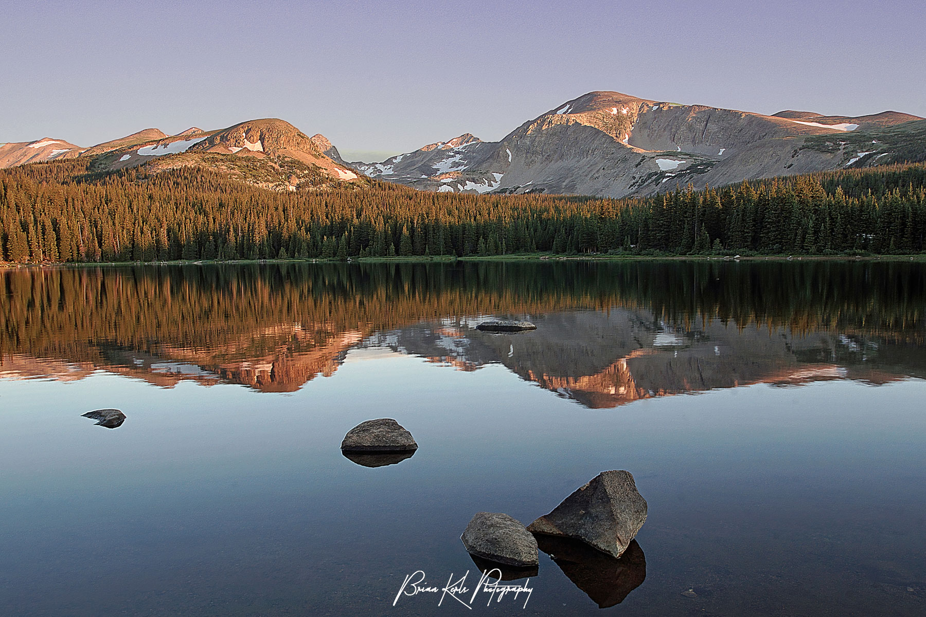 Brainard Lake in the Indian Peaks Wilderness is calm and smooth as glass at sunrise on this June morning, reflecting the surrounding mountains in the dawn light.