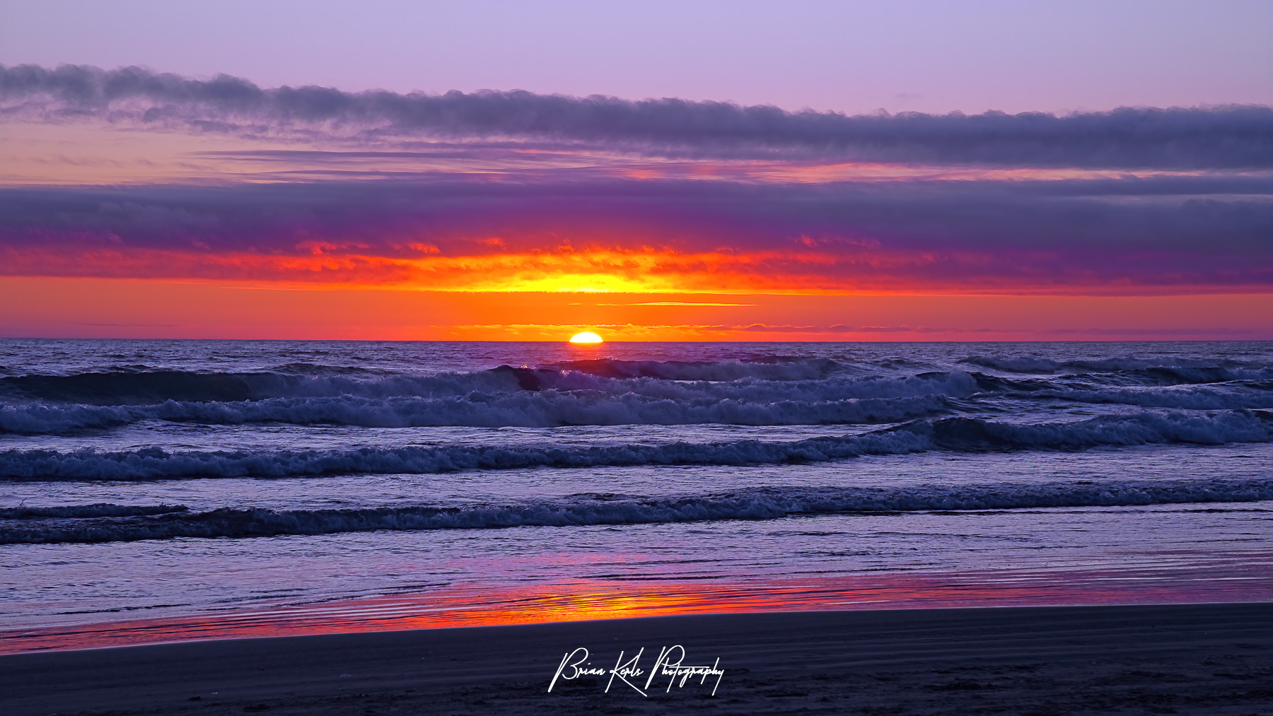 "The sun dips below the Pacific horizon casting a colorful sunset glow in the sky and on the crashing surf. Captured on a summer evening while watching the waves of the Pacific Ocean roll onto Cannon Beach on Oregon's North Coast.