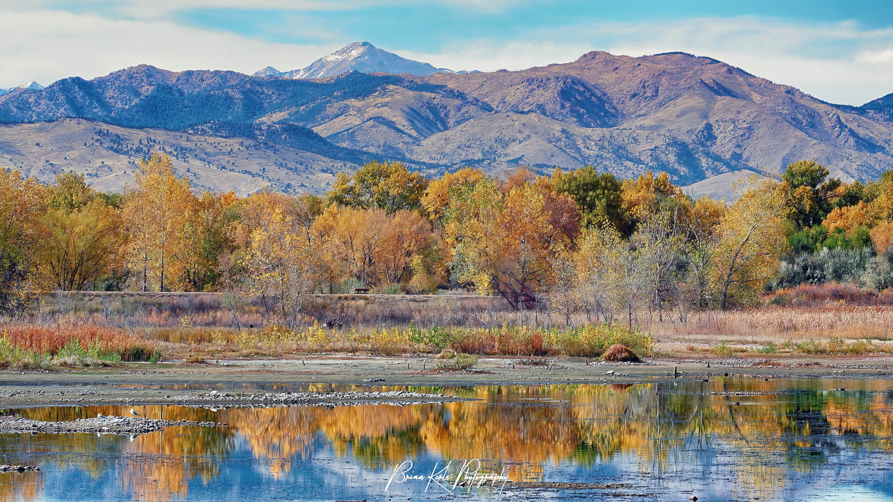 Colorful autumn trees reflected in the still water of Sawhill Ponds near Boulder, Colorado with Mt. Evans and the Front Range mountains providing a dramatic backdrop.