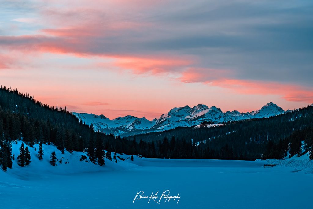 The rugged peaks of the Gore Range under a colorful winter sky painted pink by the setting sun. This view was from the shore of frozen and snow covered Black Lake at the summit of Vail Pass.
