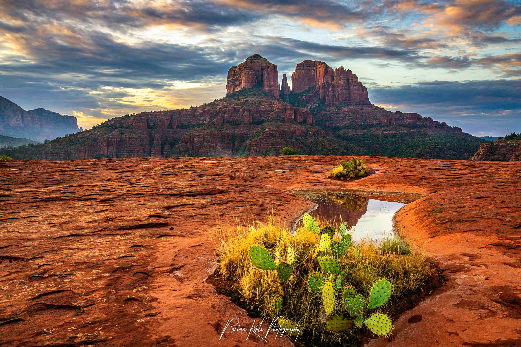 Southwest desert landscape photo print featuring Cathedral Rock in Sedona, Arizona at golden hour. Includes vivid red rock formations, cracked earth textures, desert puddle reflections, cactus, and warm sunrise tones—perfect for nature wall art, Arizona photography decor, and fine art prints of the American Southwest.