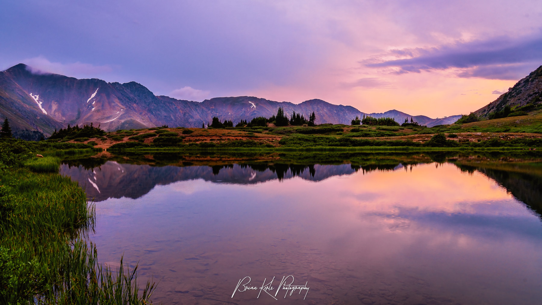 Sunset over Loveland Pass Lake in Colorado, with golden light reflecting off the still alpine waters surrounded by rugged mountain peaks and a vibrant sky.